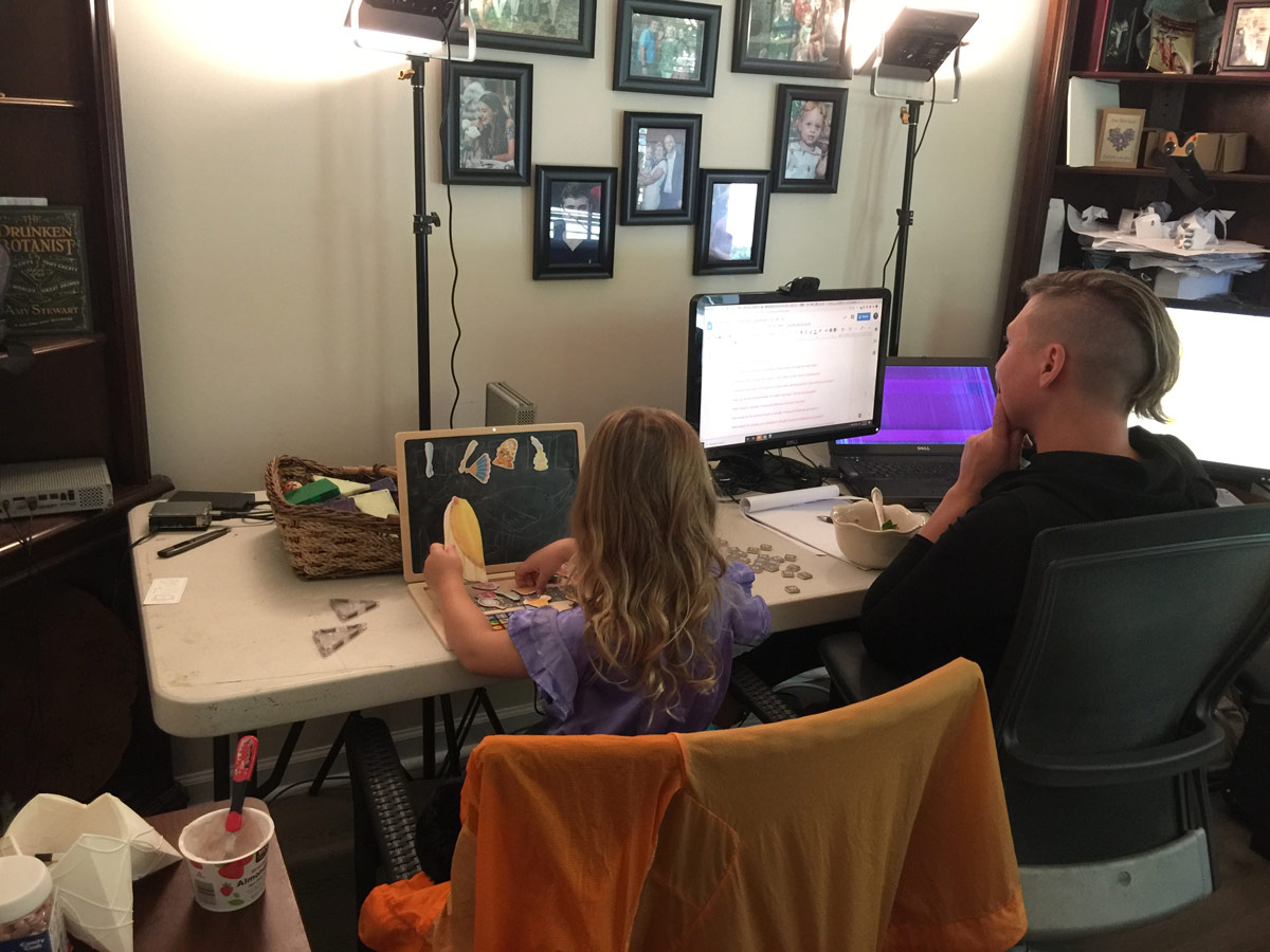 Architect Michele Gorman and young daughter sit side by side working in the architect's studio