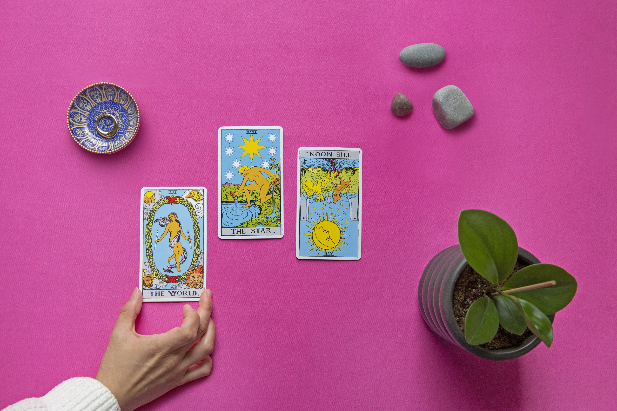A hand touches one of three cards in a tarot spread, featuring the world, the star, and the moon