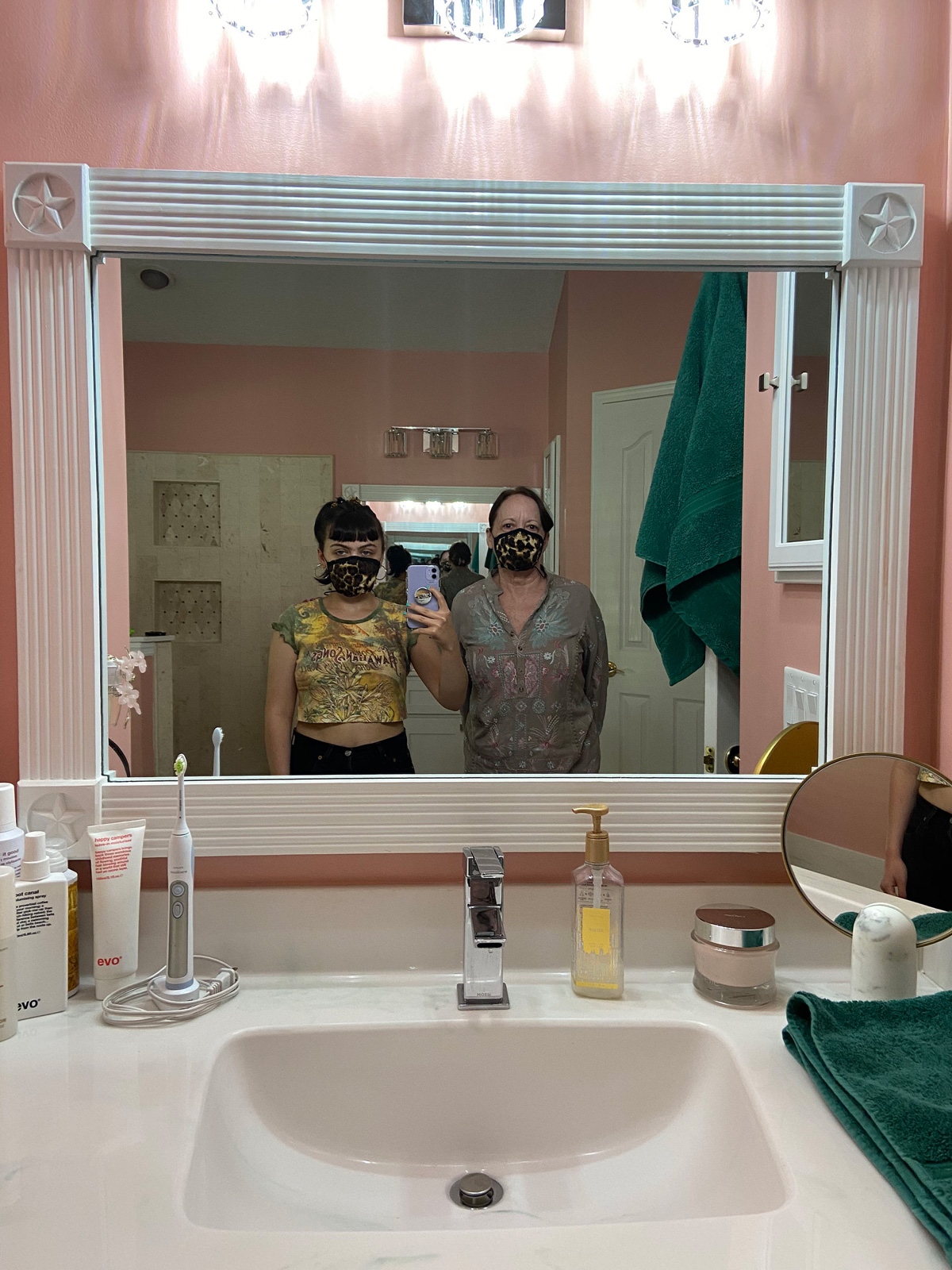 Picture of two individuals taking a selfie inside a pick bathroom, one in yellow; another in blue