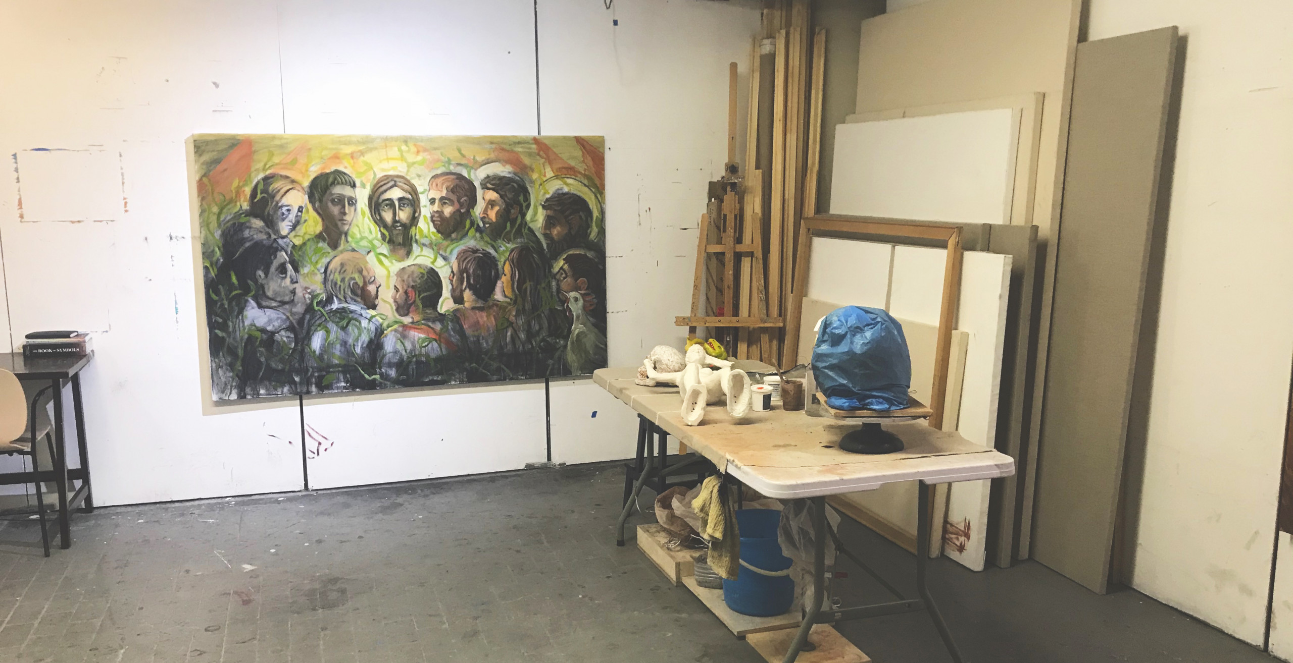 Artist's studio with large painting of people in a circle, and a table with a blue sculpture