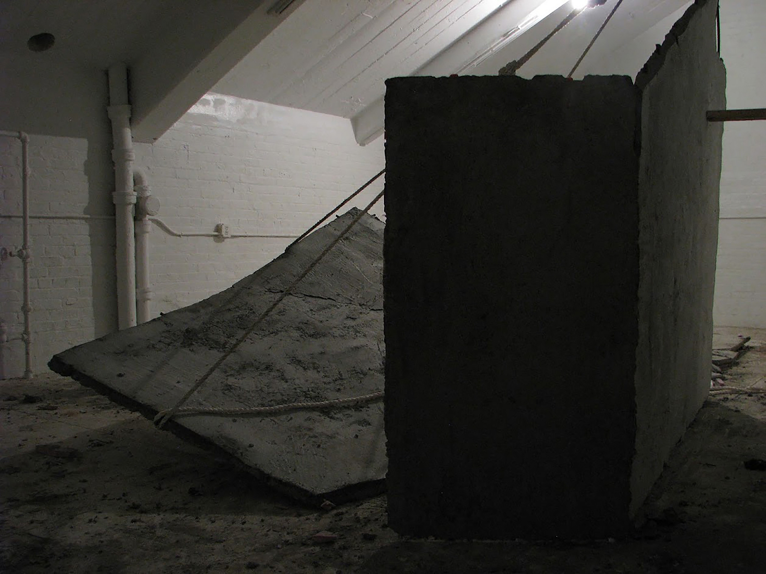 A concrete slab suspended with rope behind a shadowy wall