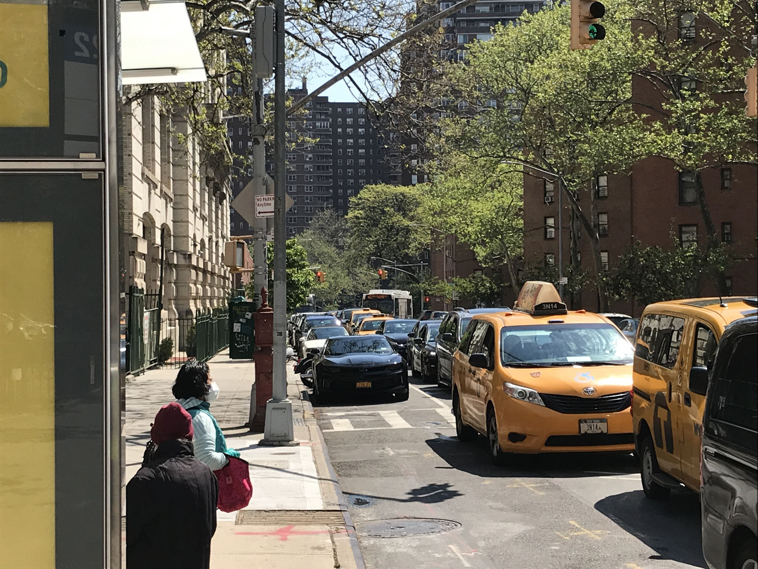 Pedestrians look at taxis and cars lined up in a city street between low towers