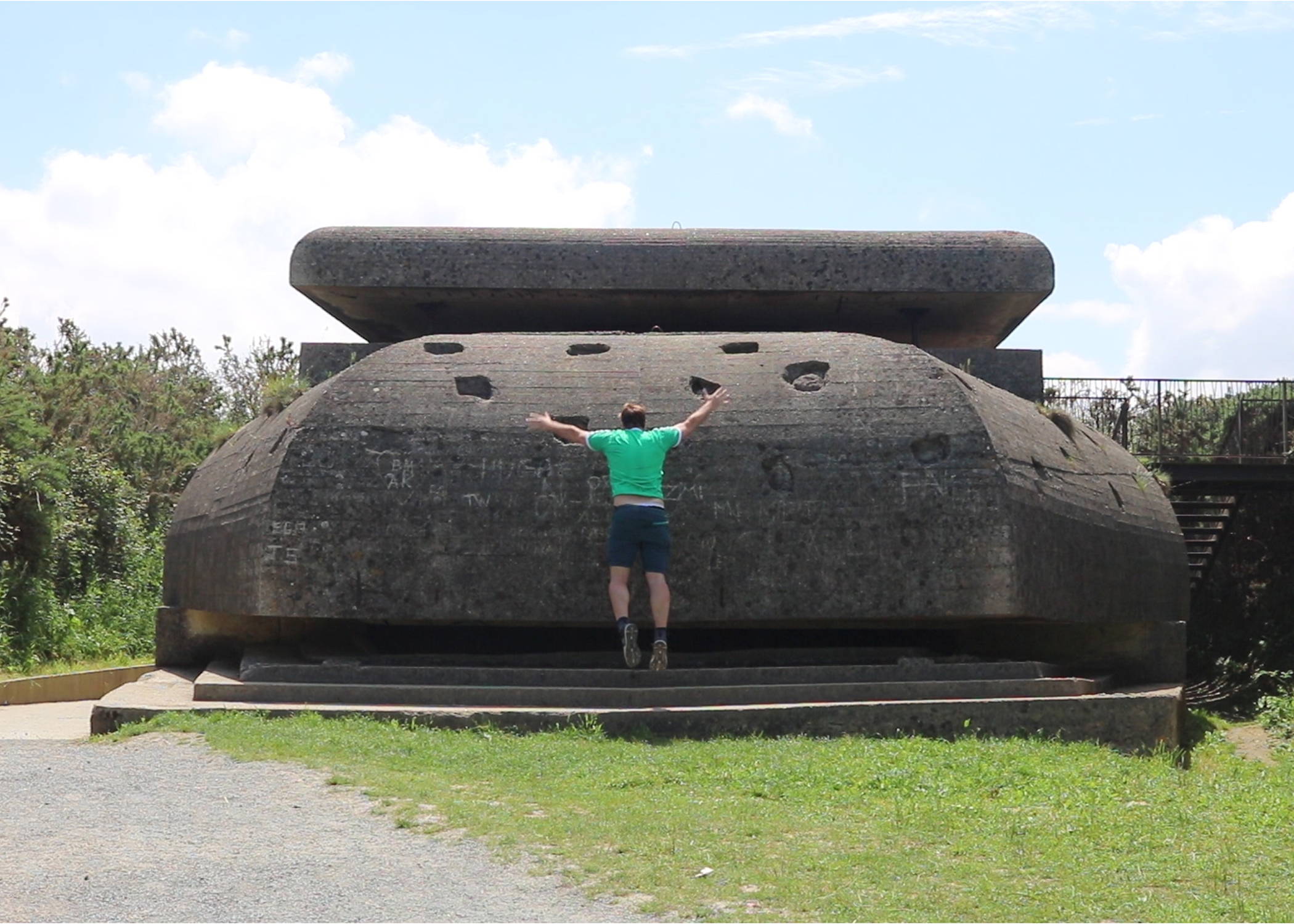 Person in green T-shirt and black shorts leaping toward stone structure