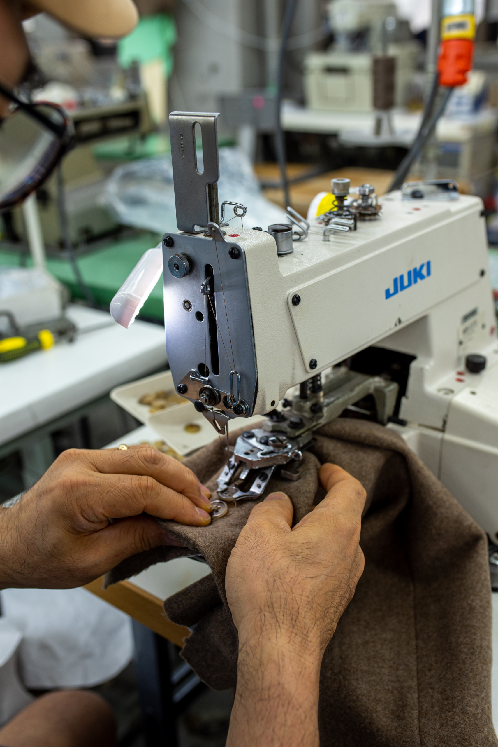 Hands moving a sleeve through a Juki sewing machine, attaching a button