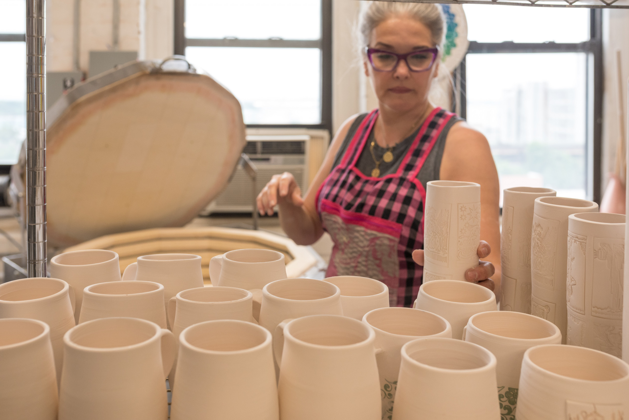 Artist places unglazed ceramic pieces on a shelf in front of a kiln