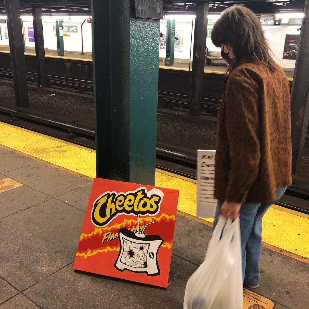 Person regards a painting of hot Cheetos on subway platform