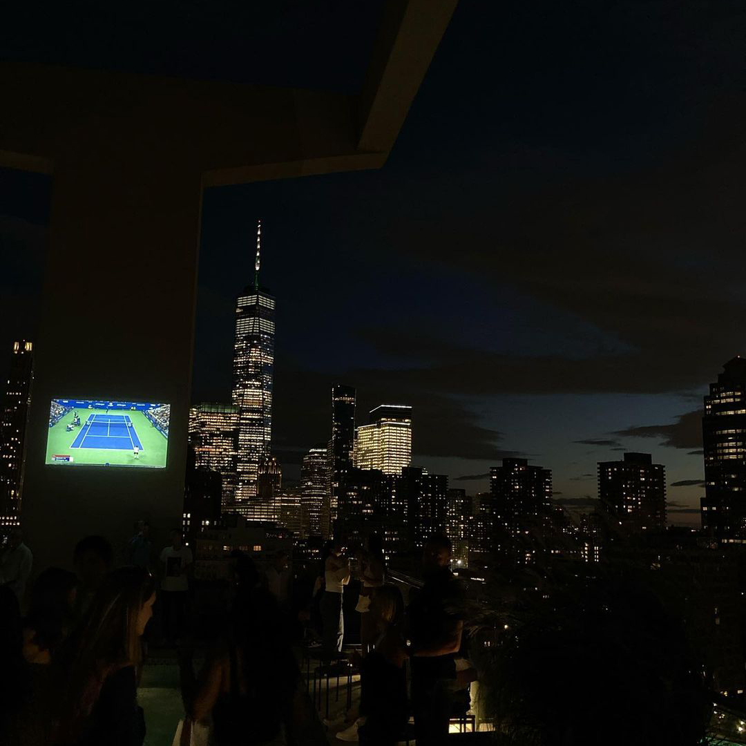 NYC skyline at night with tennis match playing on a screen