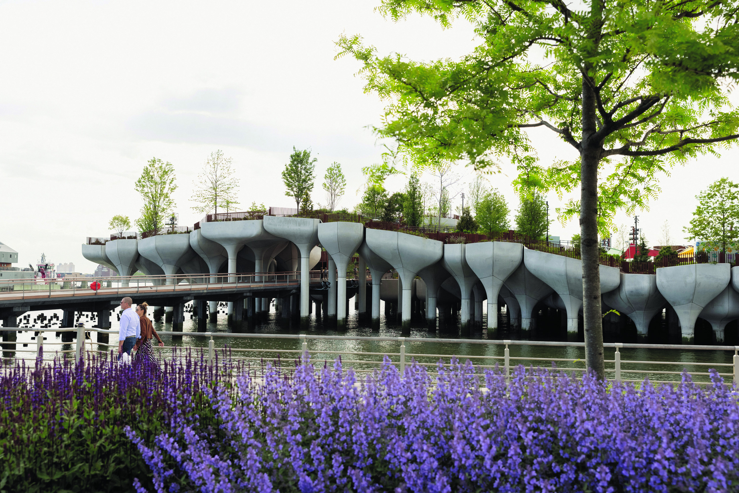Runners on a riverside path with undulating pier in the background