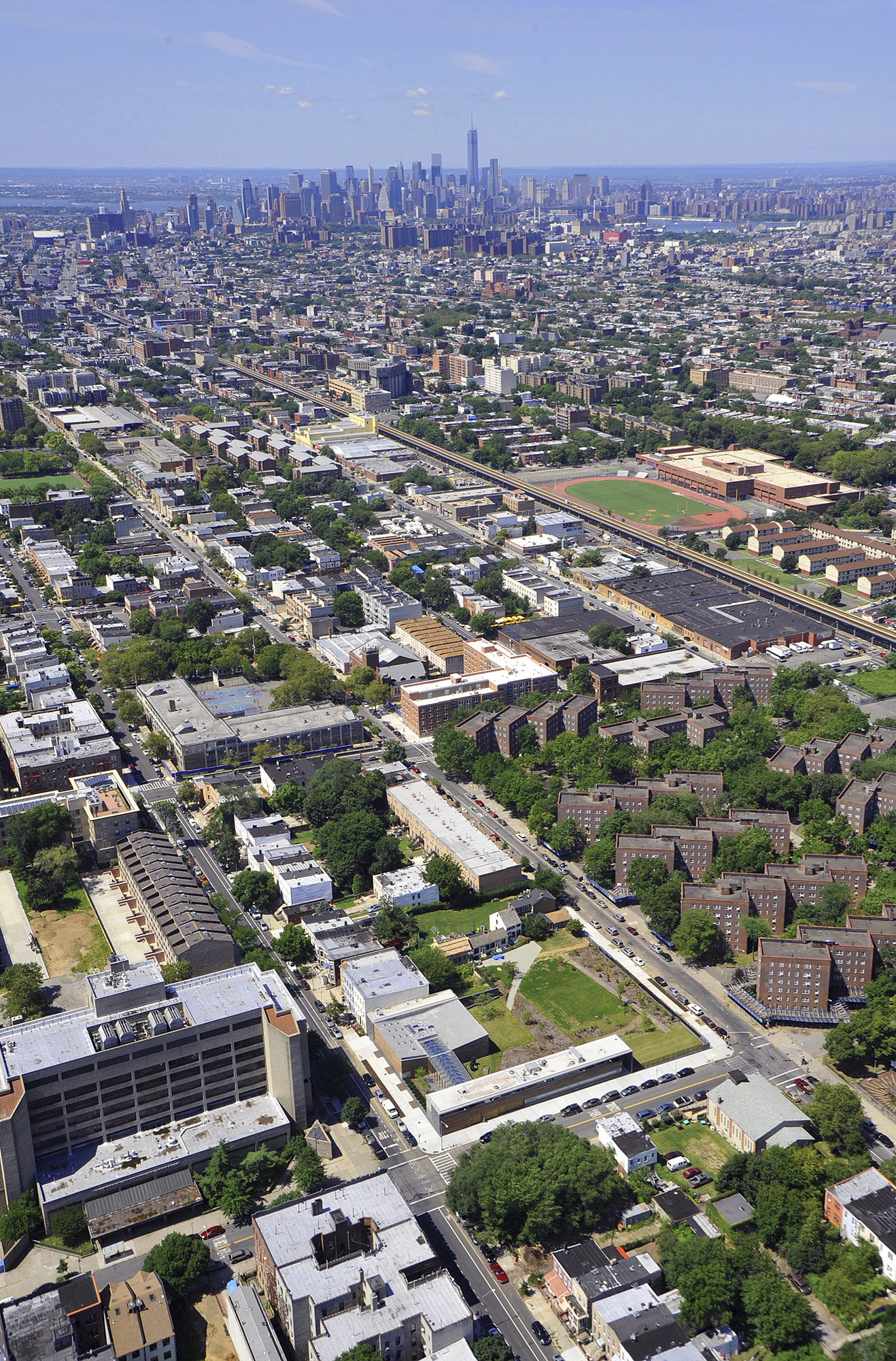 Aerial view of Weeksville Heritage Center site nested within the neighborhood grid of Brooklyn with Manhattan's skyline in the distance