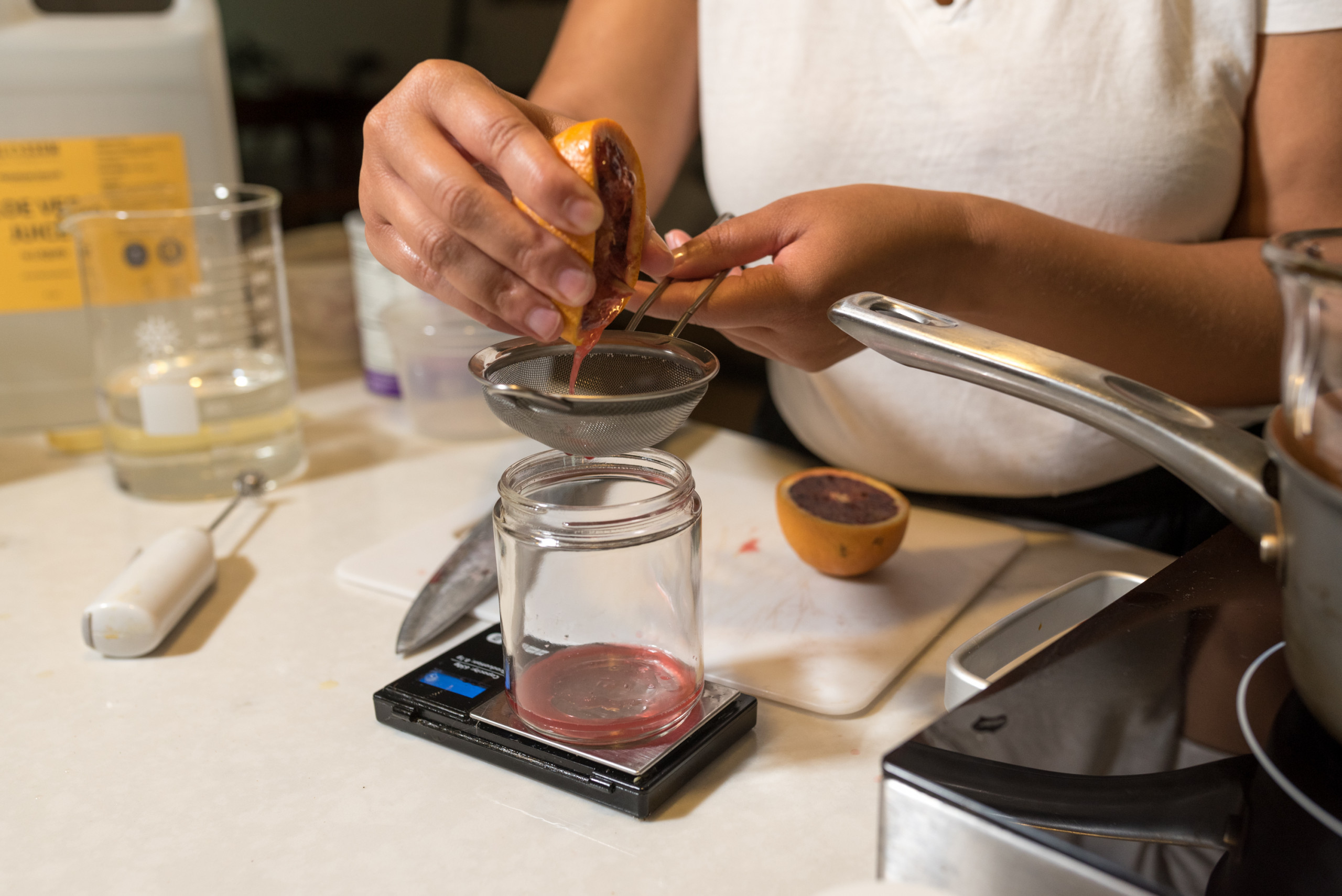 Hands squeezing juice from a blood orange into a clear glass jar