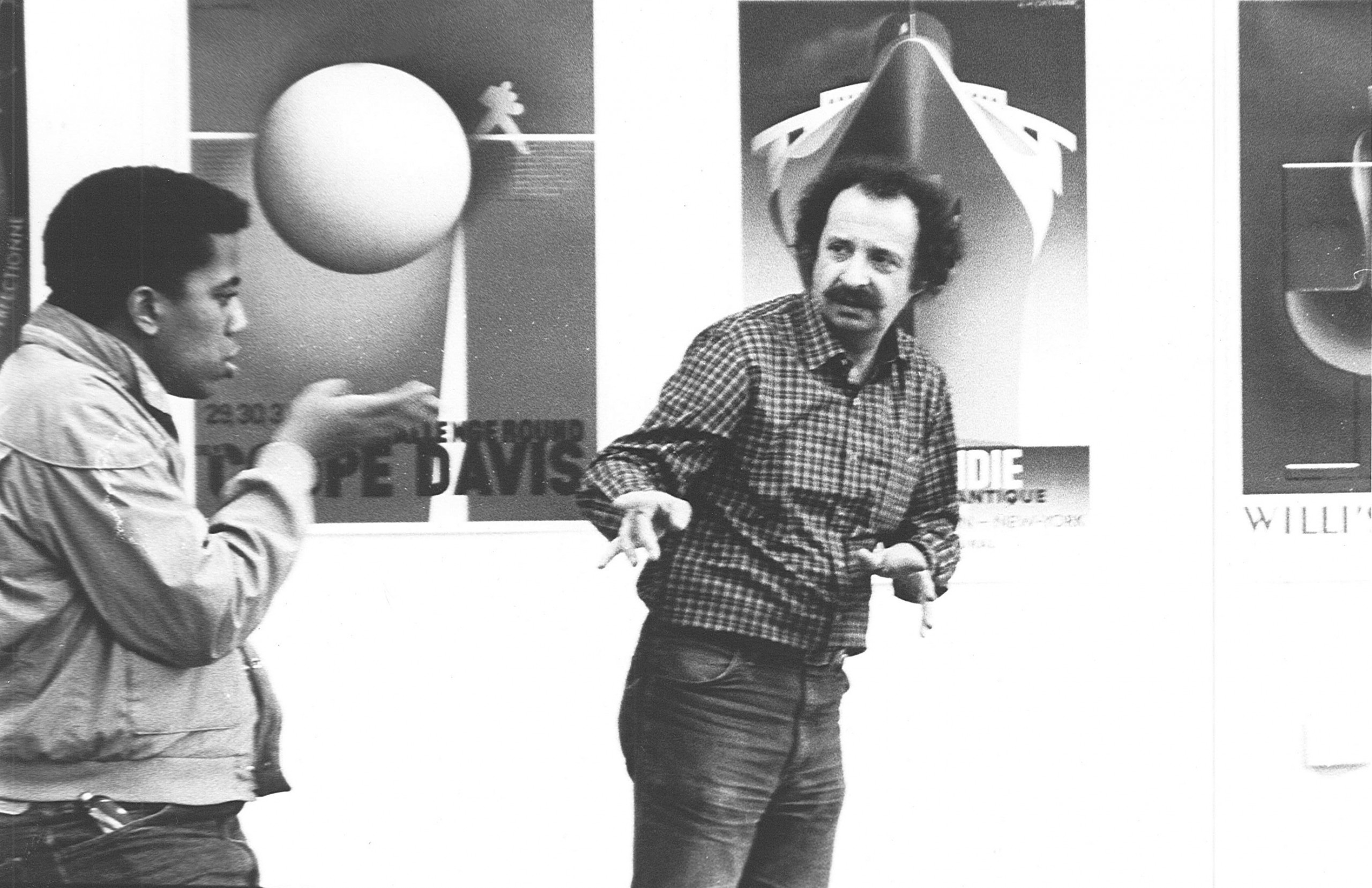 Edward Lazansky and student Thomas Reaves gesture in conversation in front of stencil-and-airbrush advertising posters