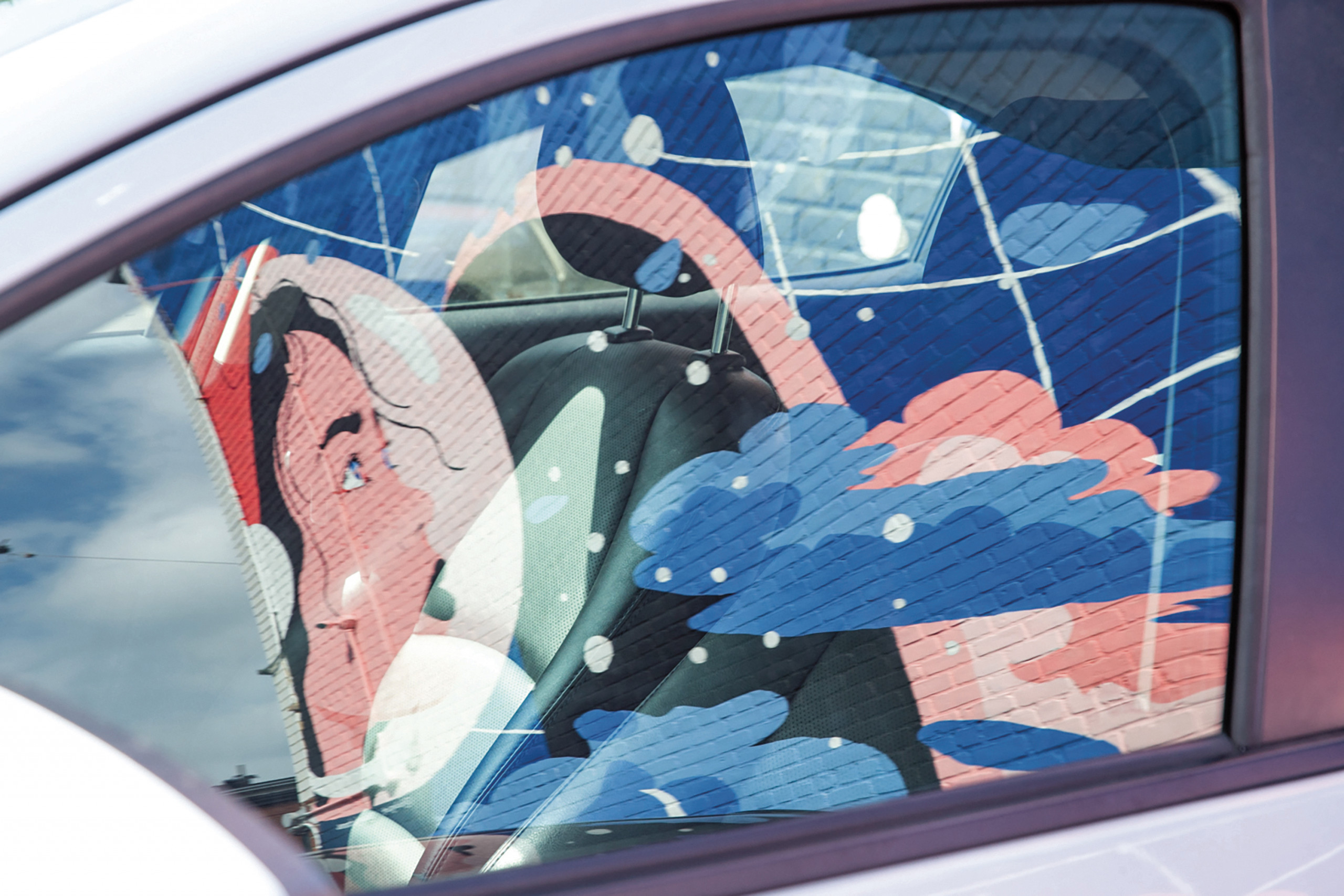 Mural with blue clouds, stars, and women's portraits reflected in car window