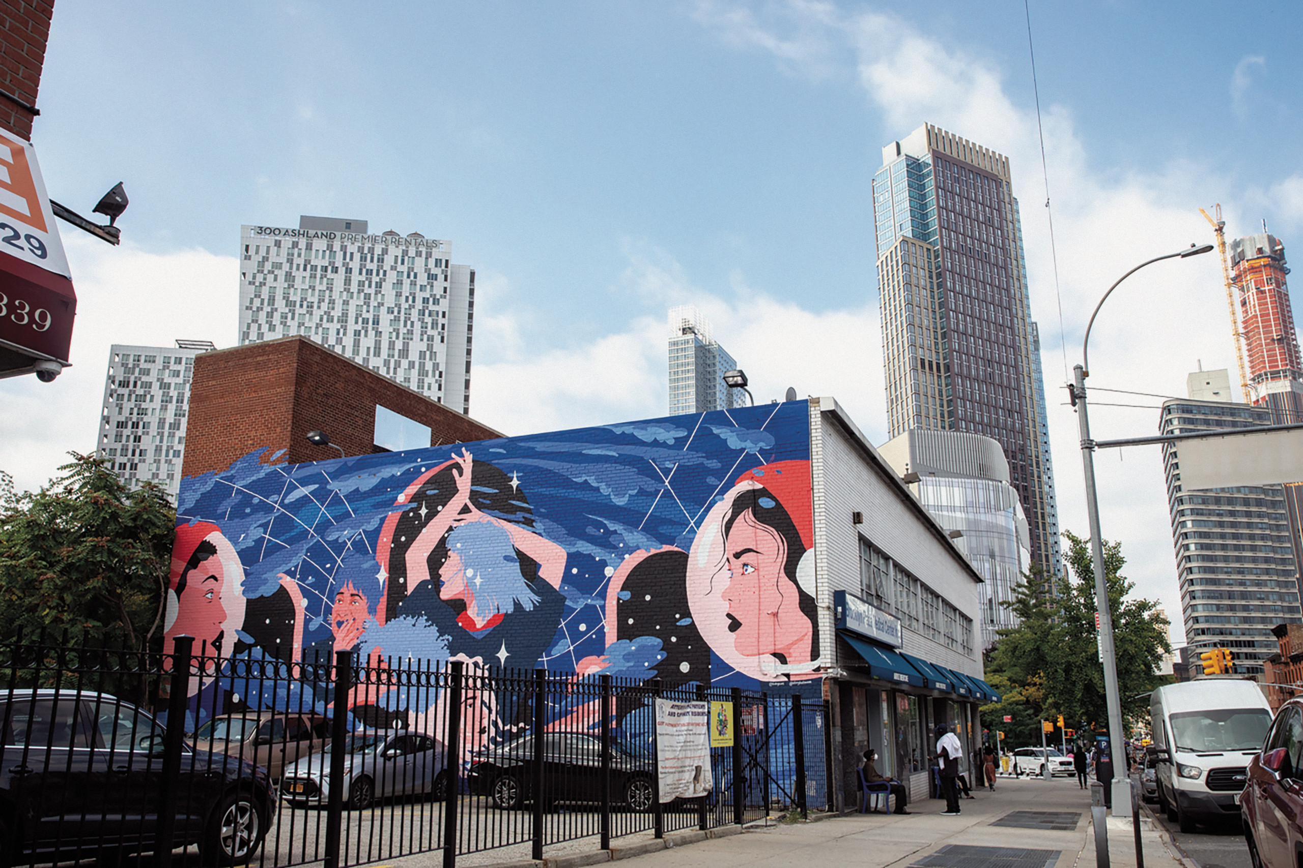 Mural with blue background and women's faces of various sizes on the side of a low building