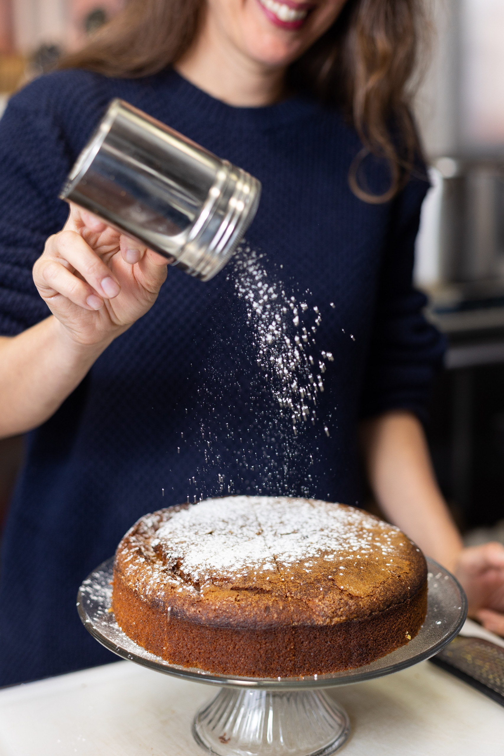 Mina Stone shakes powdered sugar on top of a round cake