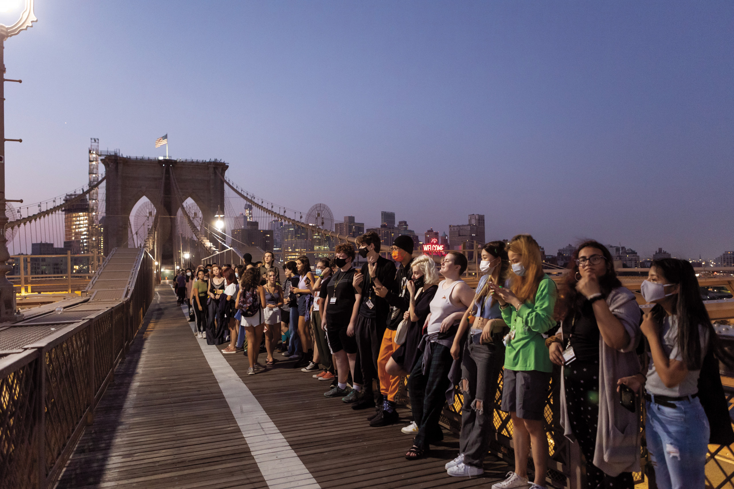 Students line up facing the breaking dawn light on the Brooklyn Bridge