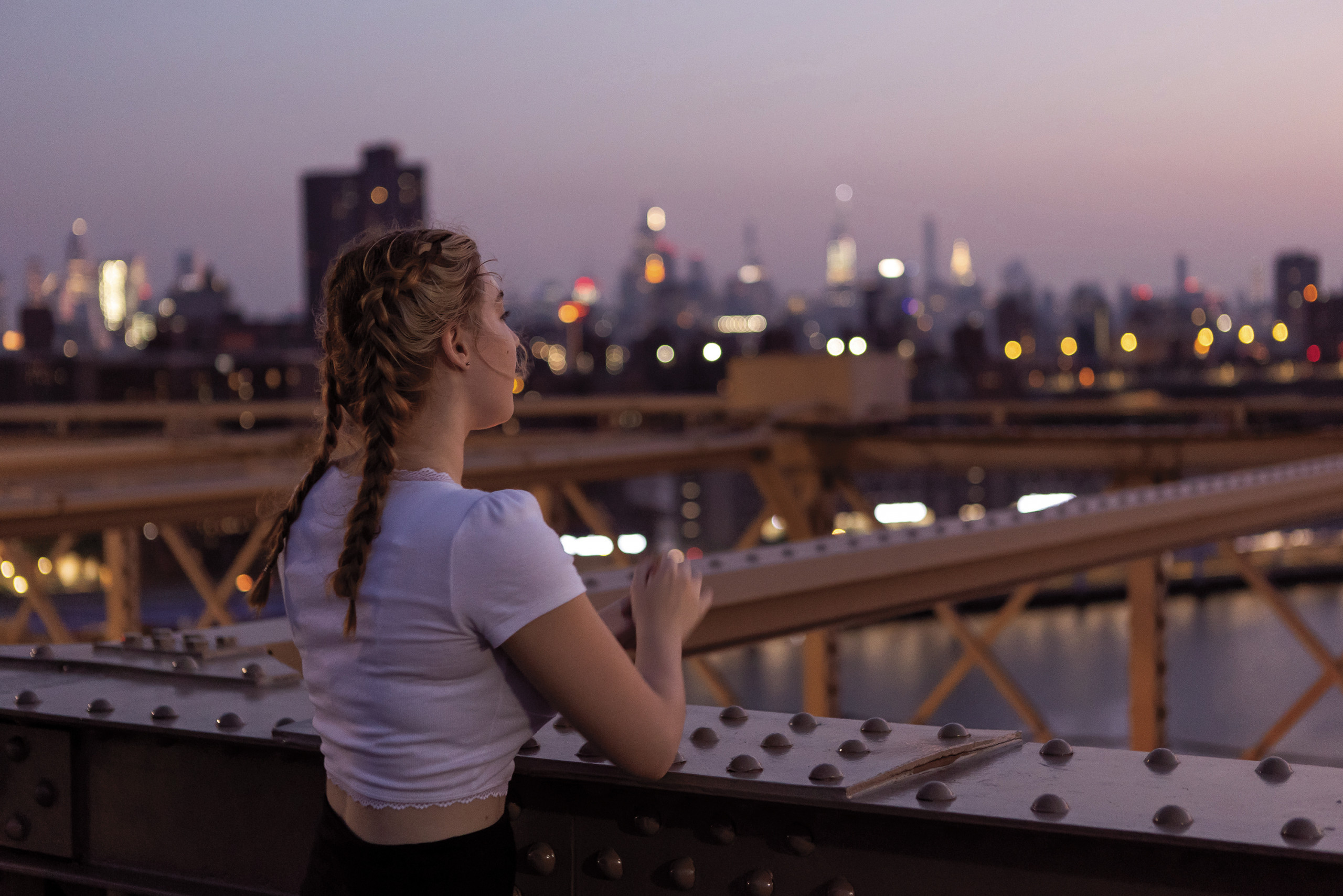 Student looks at the New York City skyline from the Brooklyn Bridge at dawn