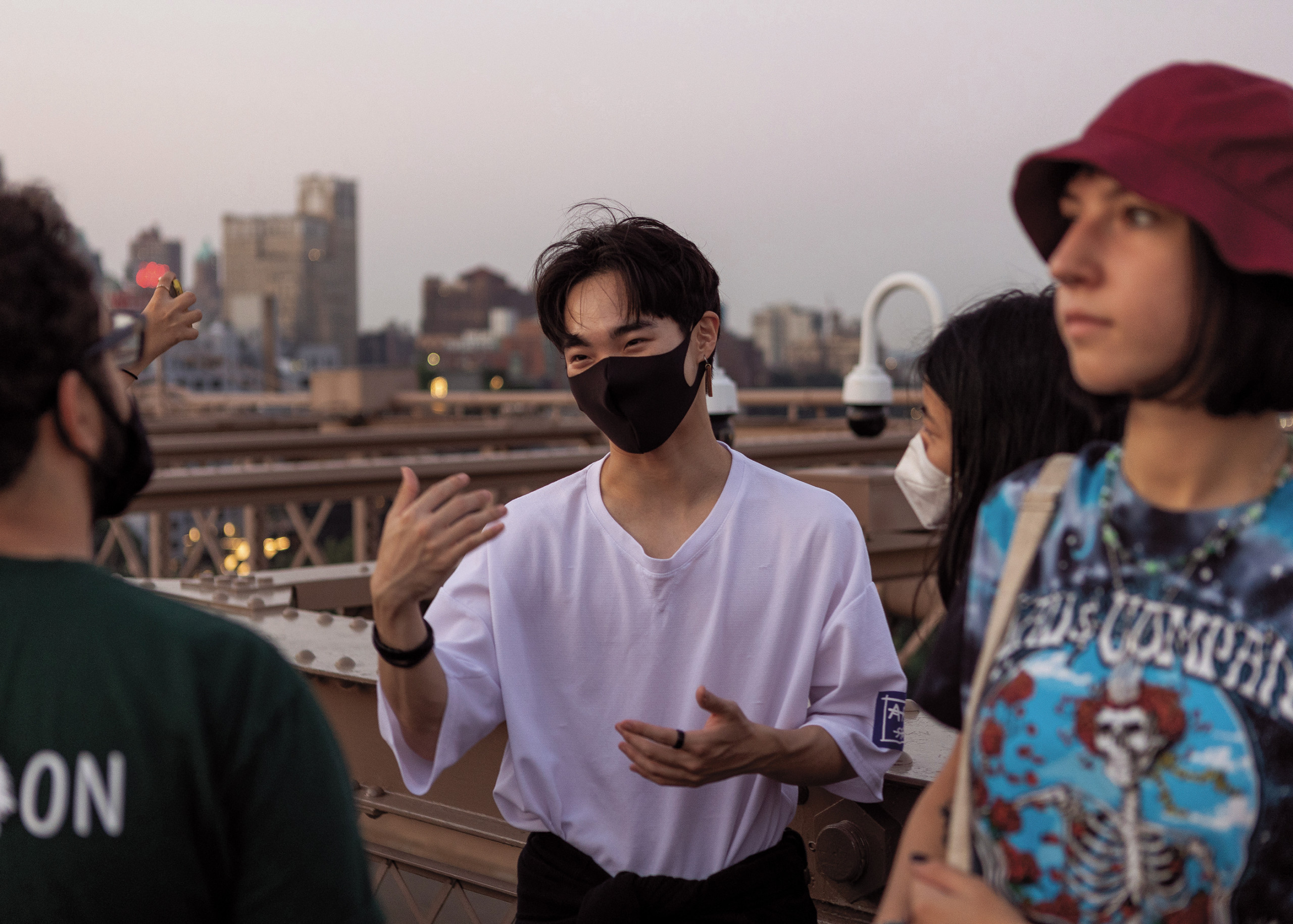 Students converse and gesticulate in the morning light on the Brooklyn Bridge
