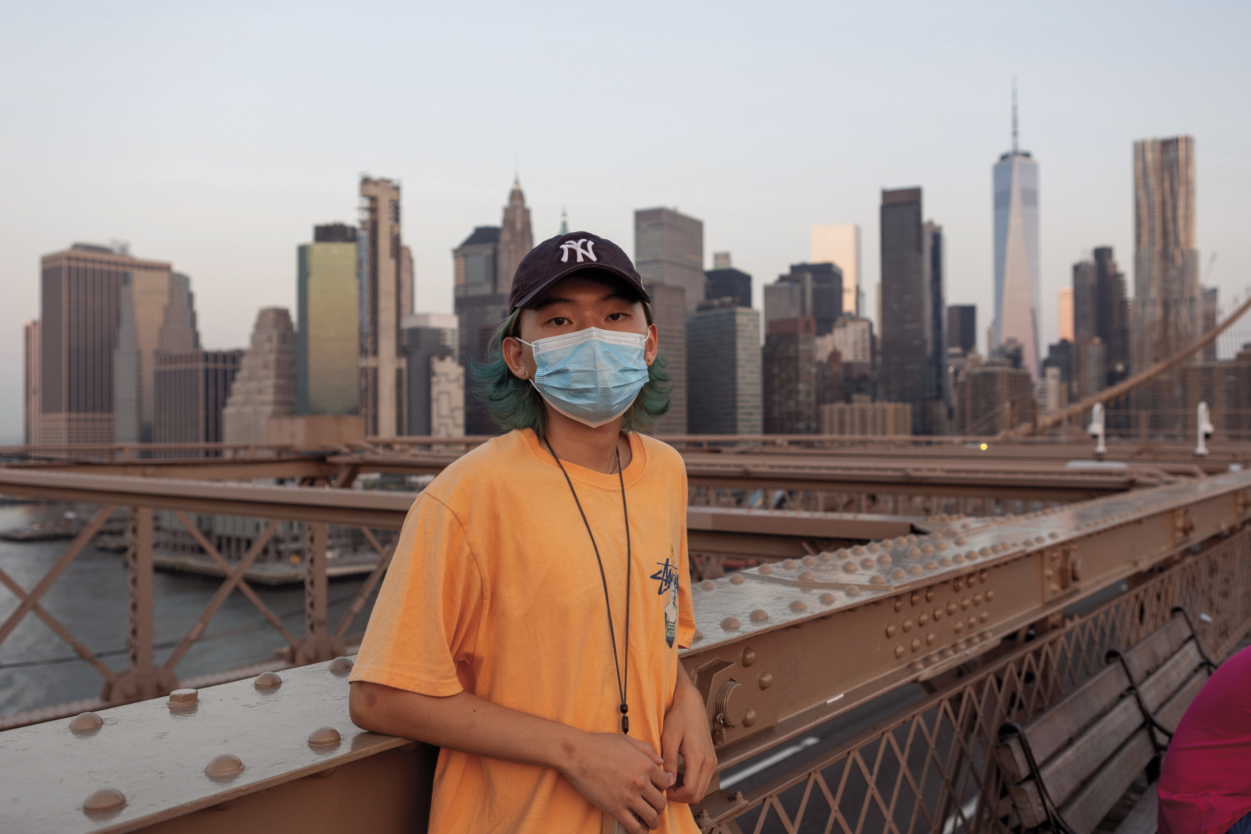 Student poses in a Yankees cap and orange Stüssy T-shirt on the Brooklyn Bridge