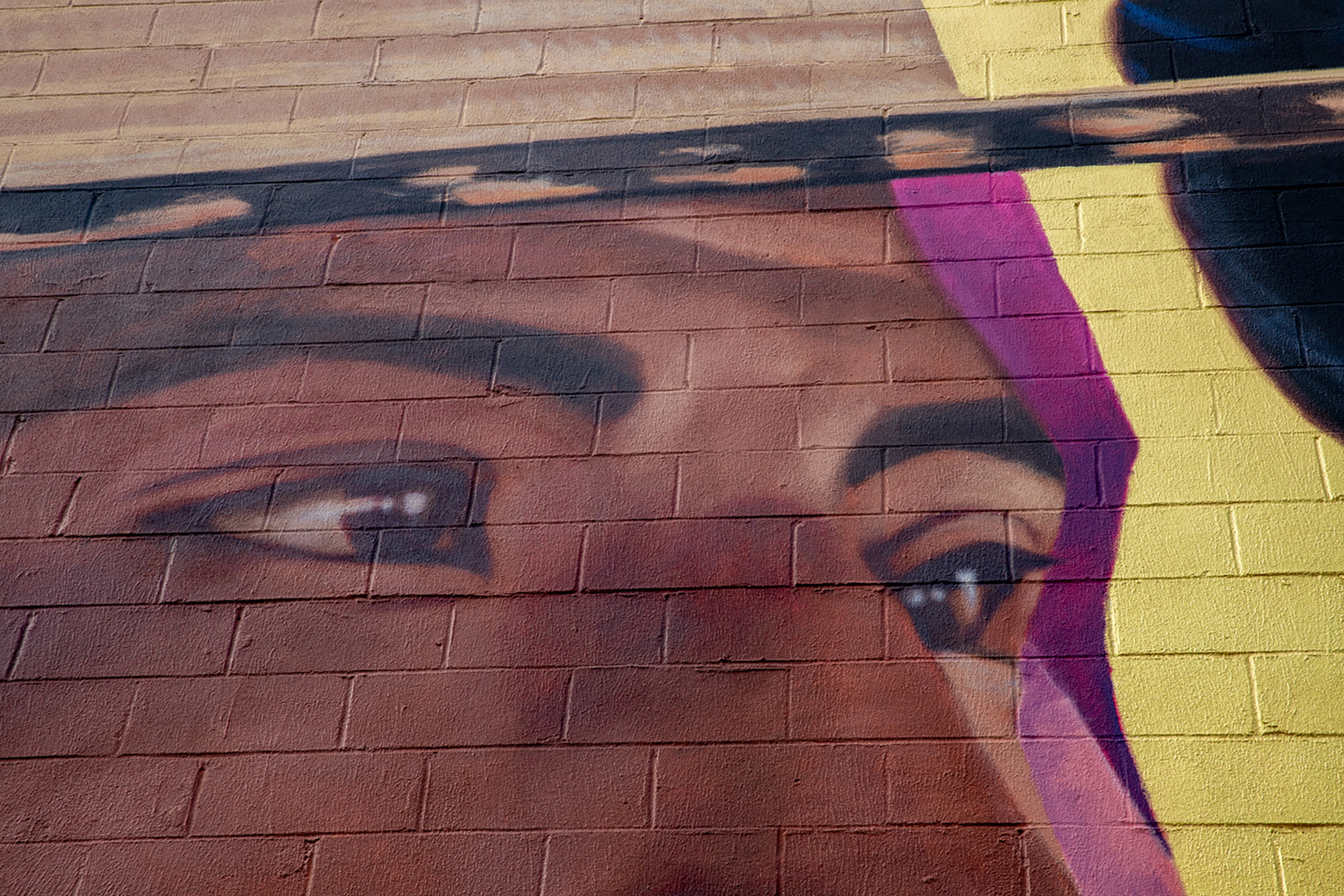 Close look at mural, showing a youth's bright brown eyes against purple and yellow background