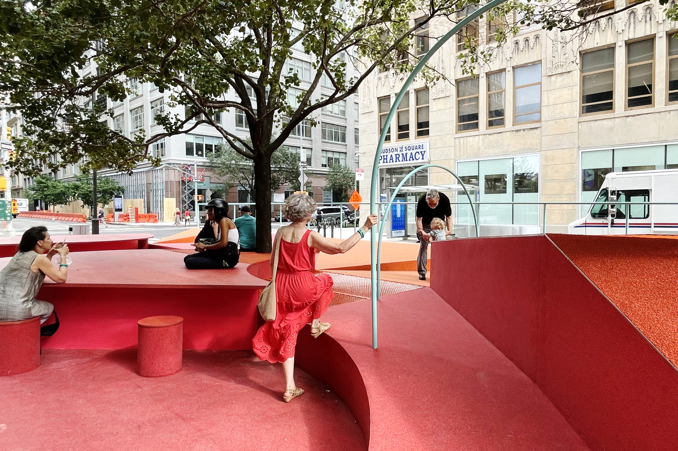 People interact with a red structure built streetside, with benches, ramps, and wide tables