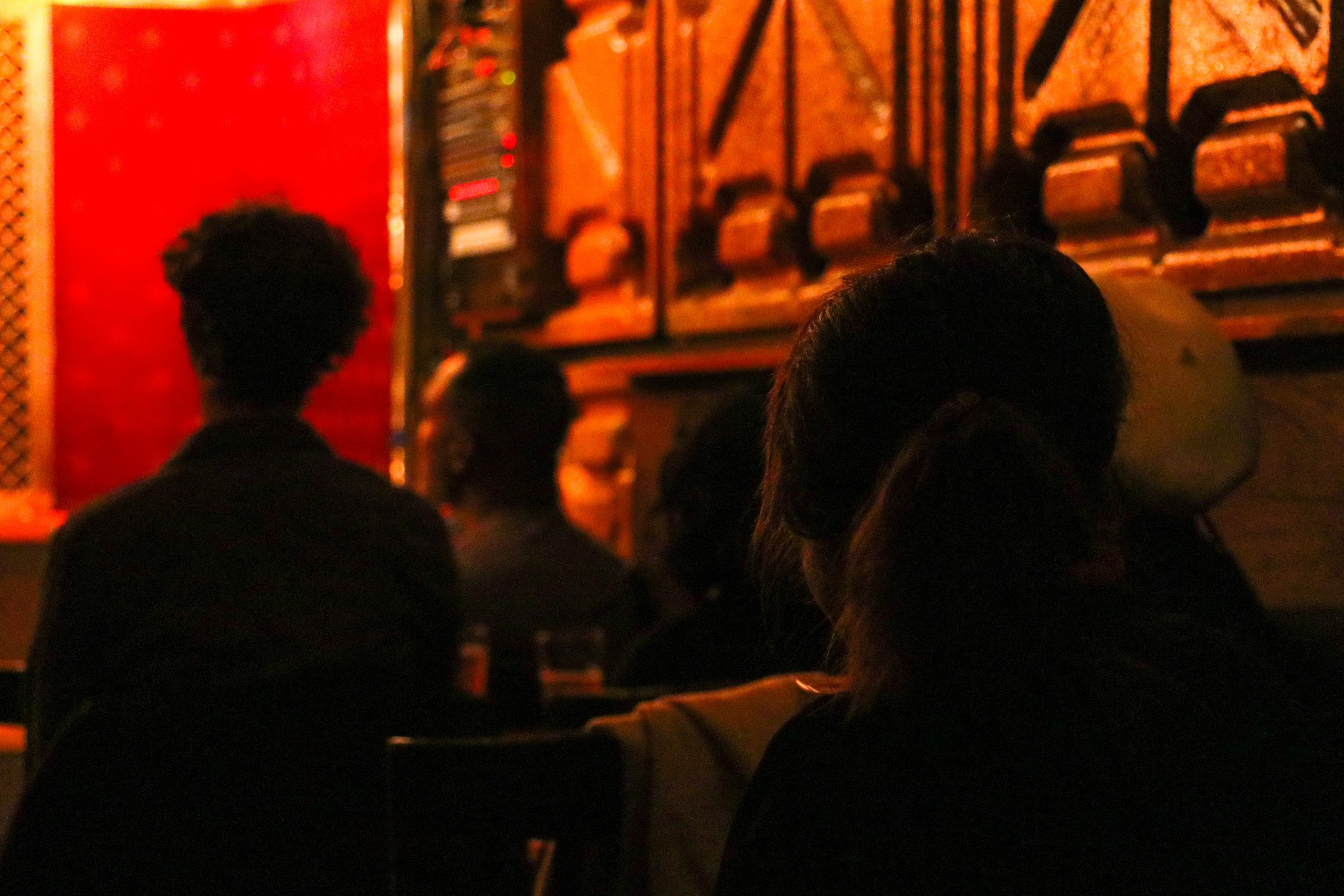 A small group of reading audience members face a red-walled stage amid dim, warm lighting