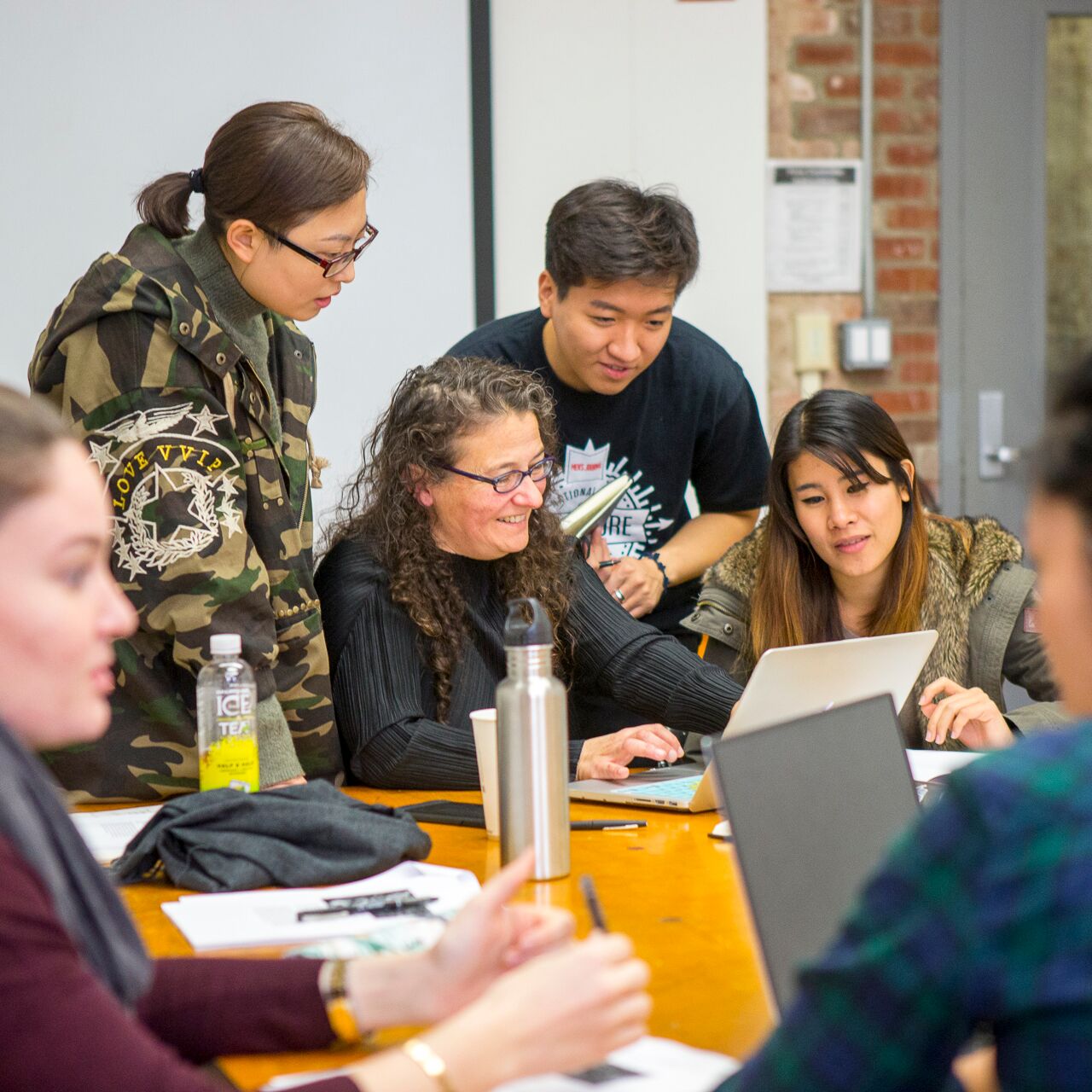 A group of students huddle around a faculty member who is showing them something on their laptop.