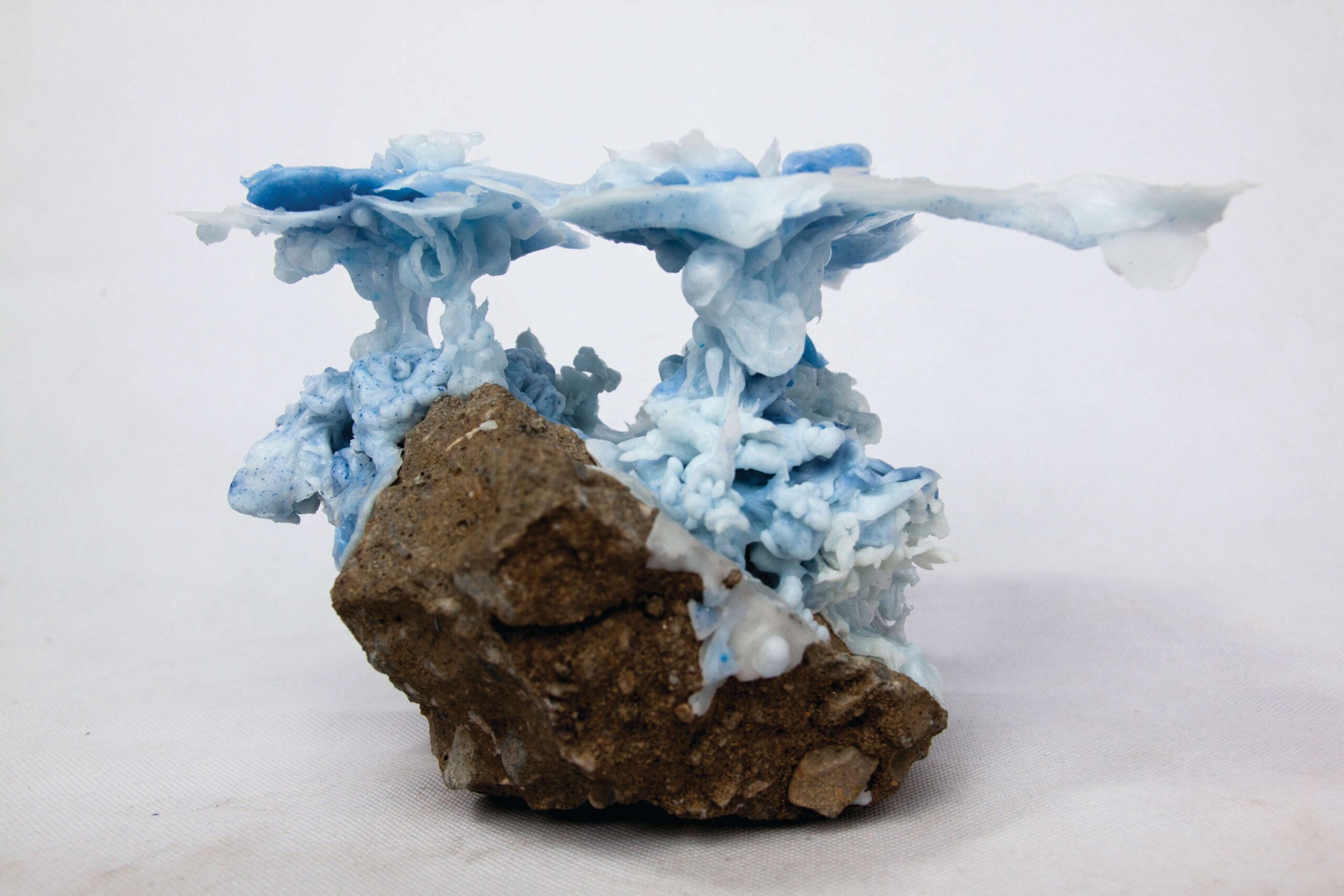 A rock formation set against a white background. There is a coral-like foam structure with blue hues growing on top of it.