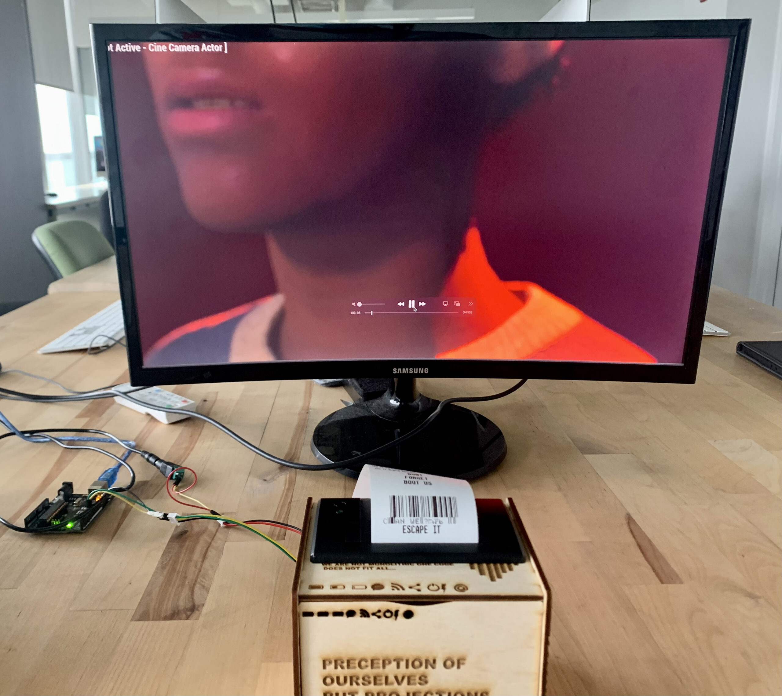 a tv monitor on a wood table, with a depiction of a black person on the screen itself, with only their chin and shoulders visible