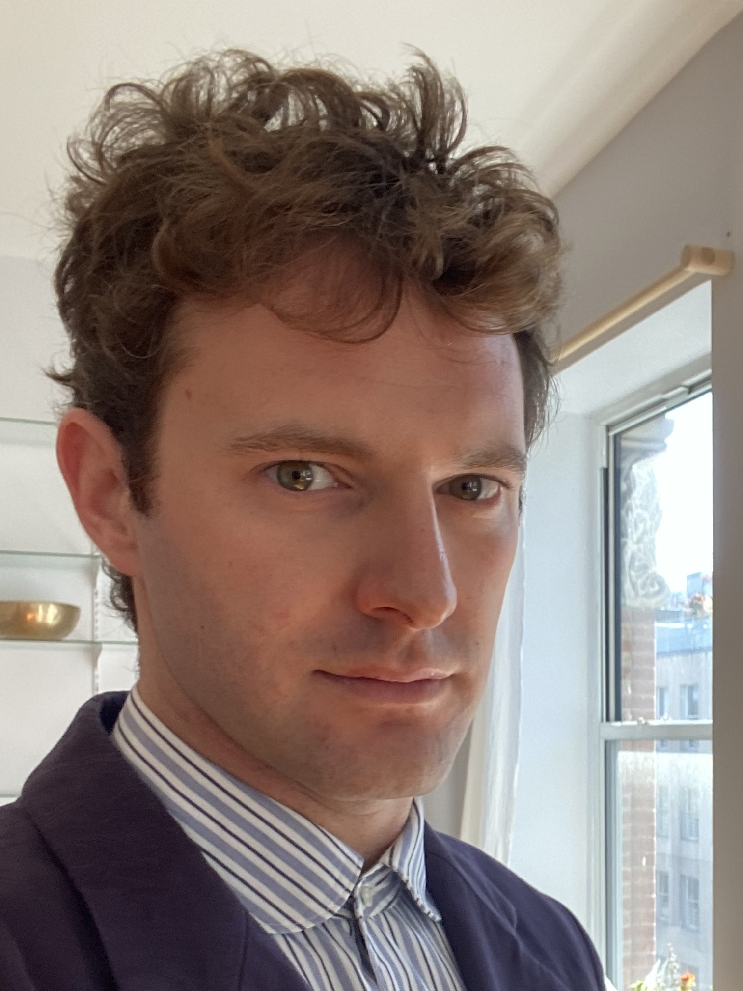 Headshot of Timmy Simonds looking at camera in a collared shirt and coat