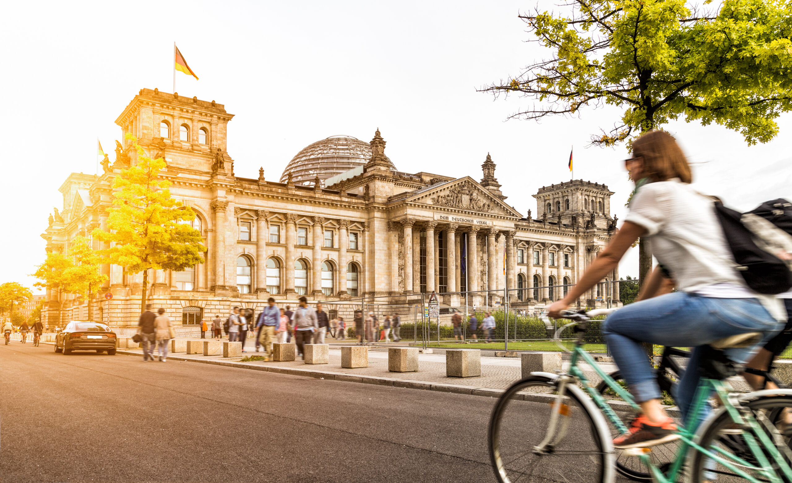 image of berlin germany, with woman riding bike by tree in foreground, large municipal government building in background