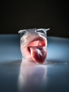A surreal and hyperrealistic artwork featuring a tongue protruding from a sealed transparent plastic wrapper. The object is placed on a reflective surface with a soft gradient background transitioning from dark to light. The image evokes a sense of ambiguity and intrigue, blending organic and artificial elements.