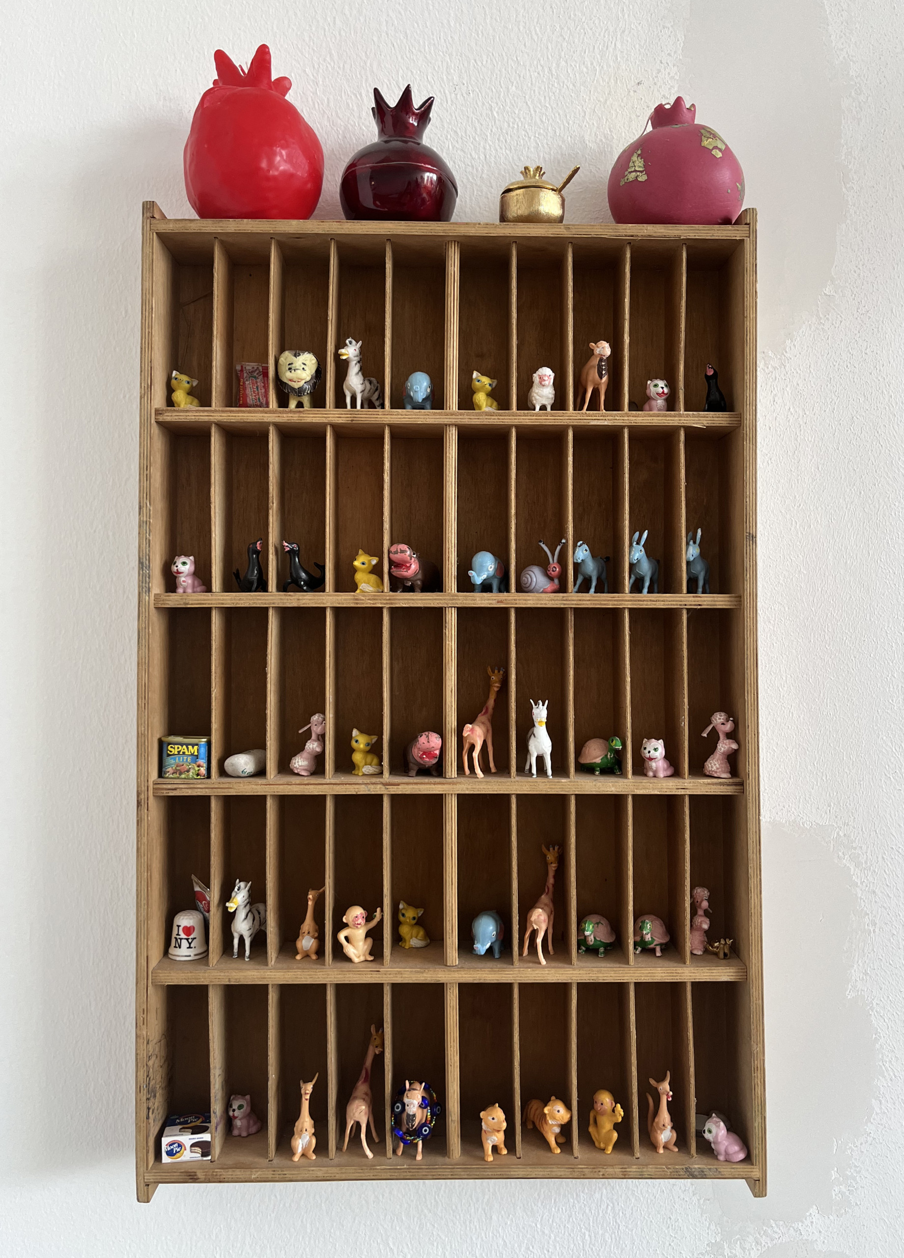 Curio cabinet with miniature animals perched on small shelves and several sculpted pomegranates sitting on top