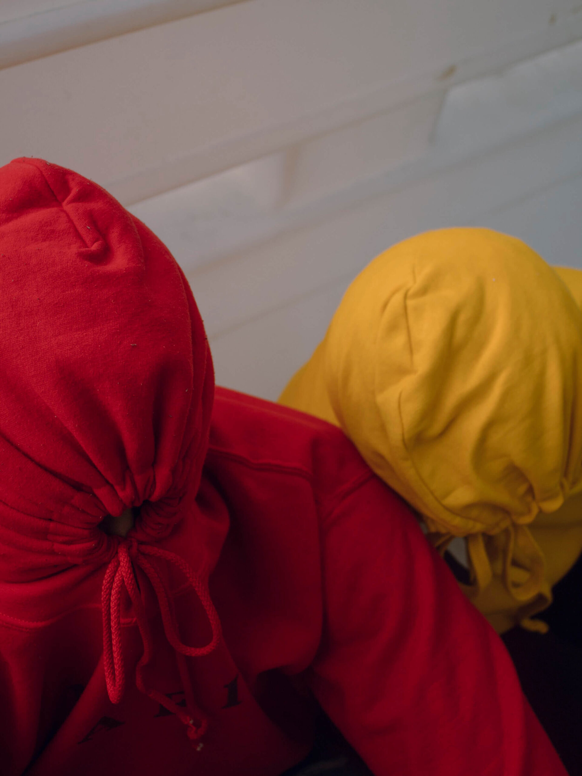 A an image of two people wearing red and yellow hoodies. The hood of their jackets is tightened as to cover their faces.