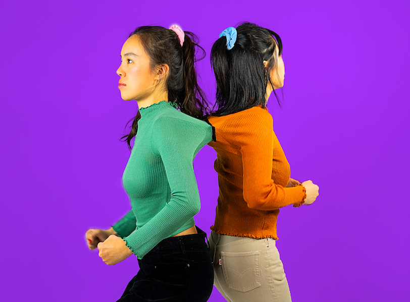 two women attached with velcro by the shirts, against a deep blue background