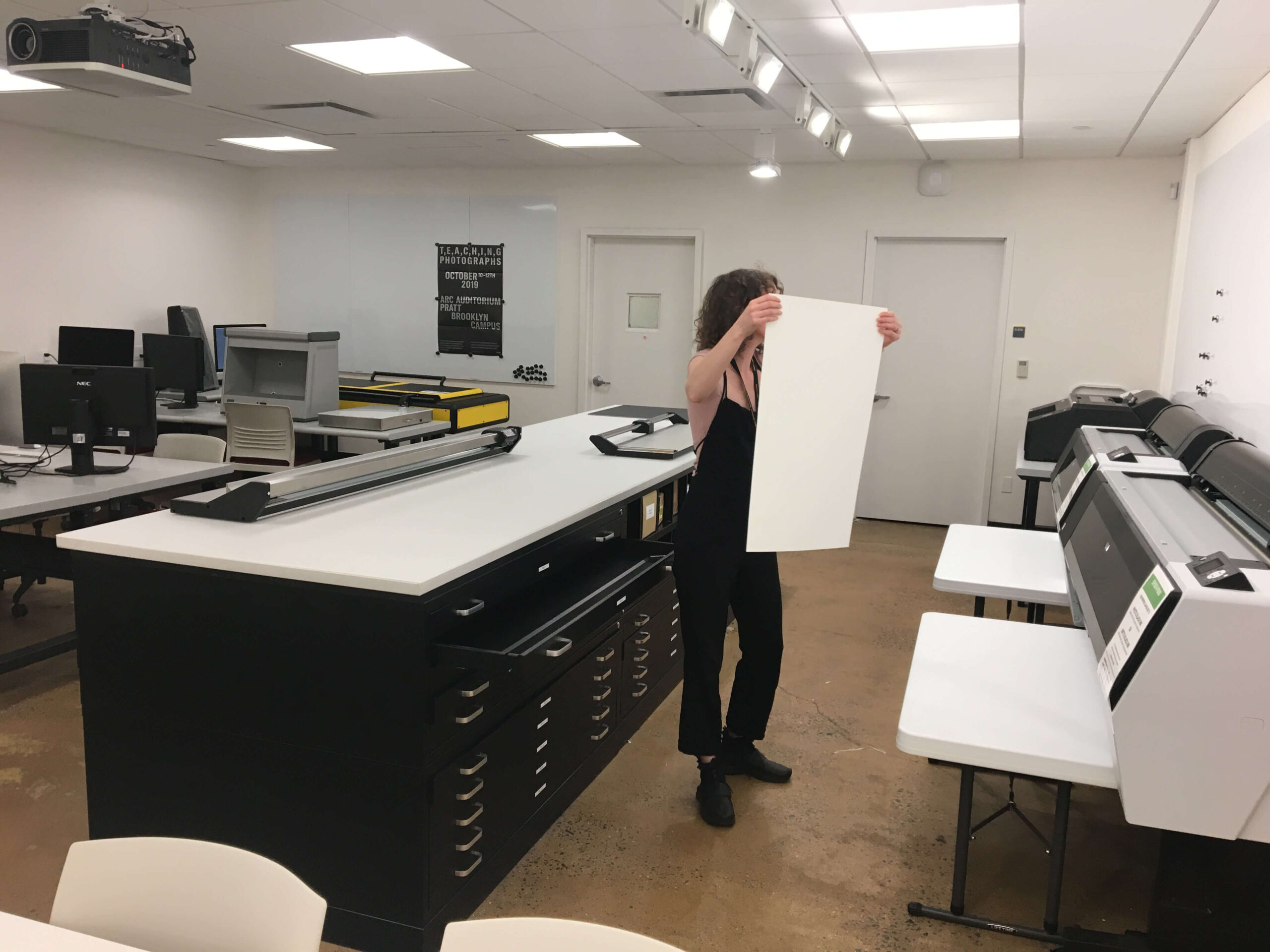 A student holds a large, printed photo inside a photography studio. The poster is covering the students face.