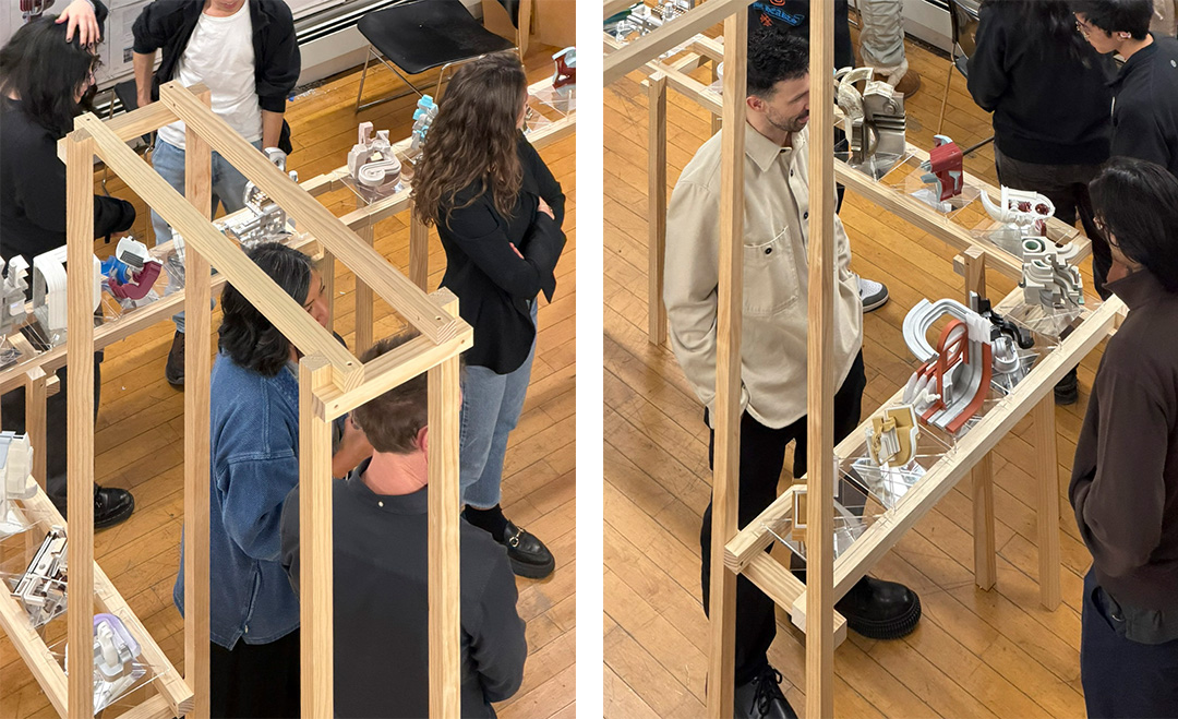 Two vertical photographs show people viewing architectural models displayed inside tall wooden frames with clear protective panels. Individuals stand around the structures, observing and discussing the detailed miniature designs placed on wooden floors in a studio or gallery setting.