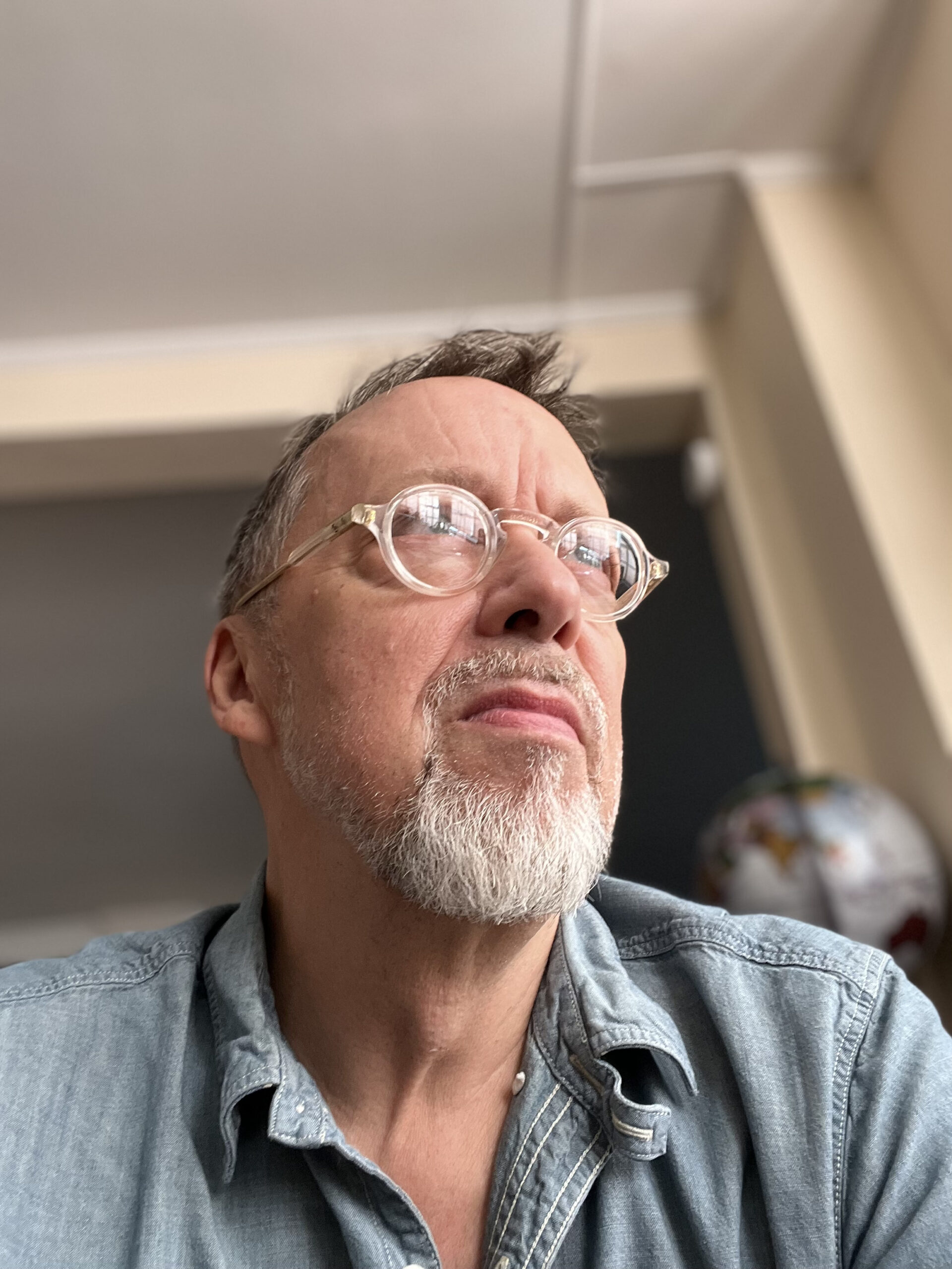 Ira Livingston looks away from the camera. Headshot is taken from a low angle and there is a chalkboard in the background