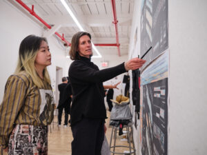 A student attentively observes an alumna describe her work in a gallery.
