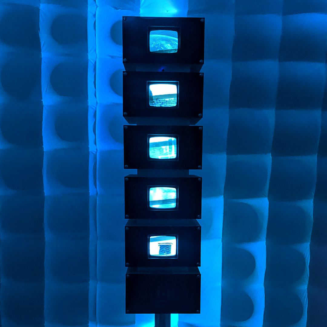 five small monitors in black box cases, stacked vertically, in front of what resembles sound paneling