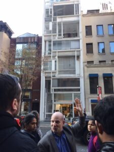 professor pointing at and discussing three floor ultra modern apartment building in new york city to large group of students, walking