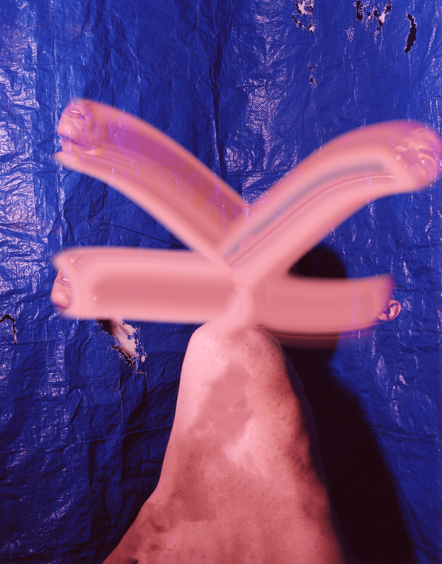 A long exposure photograph of pin neon lights making a sculpture-like shape. There is a blue tarp behind the lights.