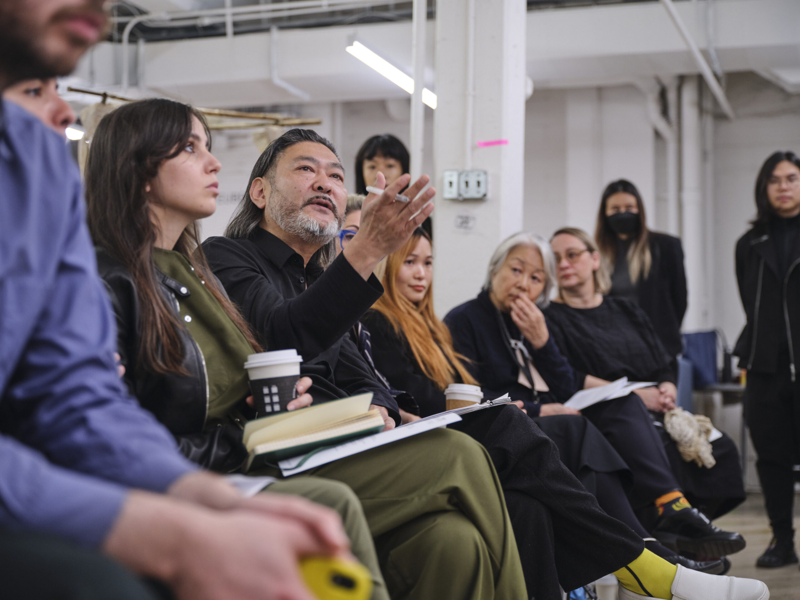 A group of people sits in a classroom as they watch a presentation. One of the participants is motioning with his hands as he asks a questions