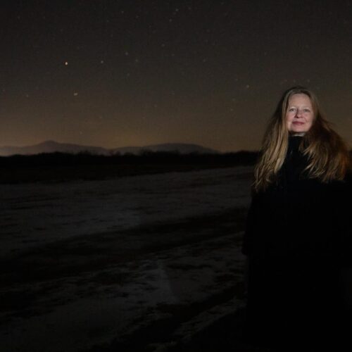 Samantha Hunt stands in the dark with her face illuminated by flash as she smiles towards the camera.