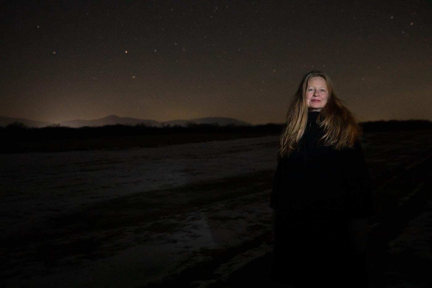 Samantha Hunt stands in the dark with her face illuminated by flash as she smiles towards the camera.