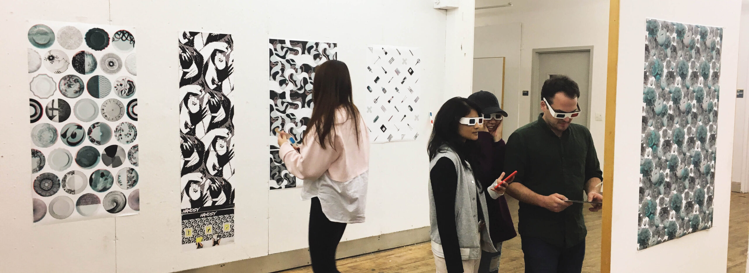 A group of people wearing 3D glasses at an art gallery look at art hung on white walls.