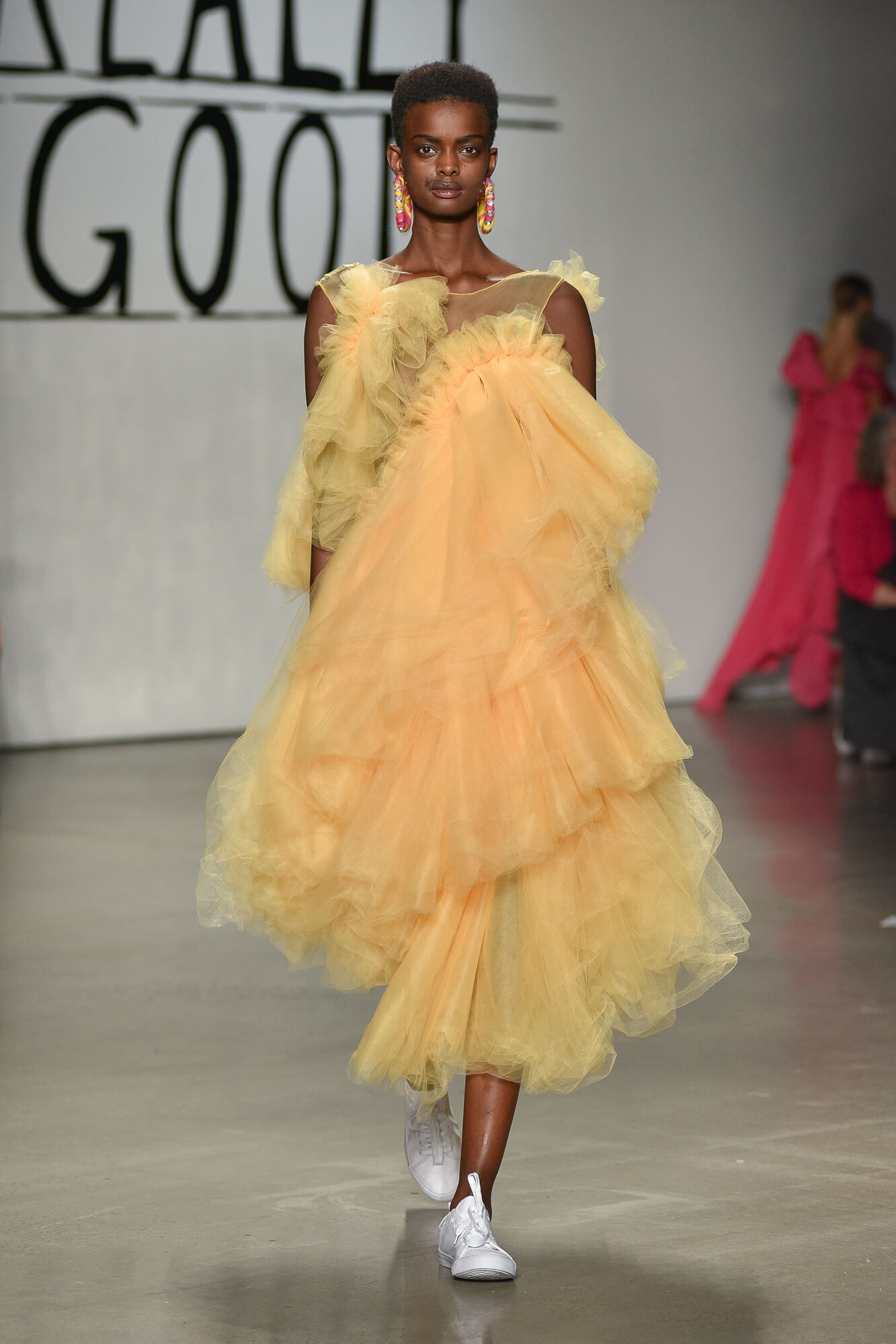 A model walks down a runway wearing a yellow dress with multiple layers of translucent fabric.