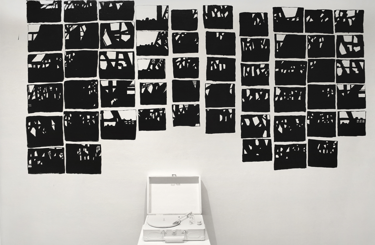 A white record player with multiple black abstarct paintings on the wall against it