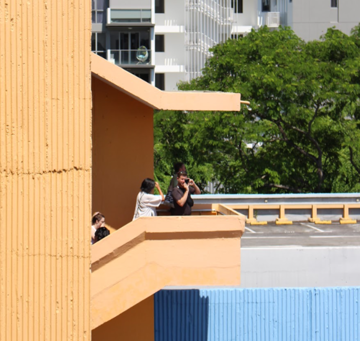 People stand on an outdoor stairwell overlooking a city. One is taking a photo.