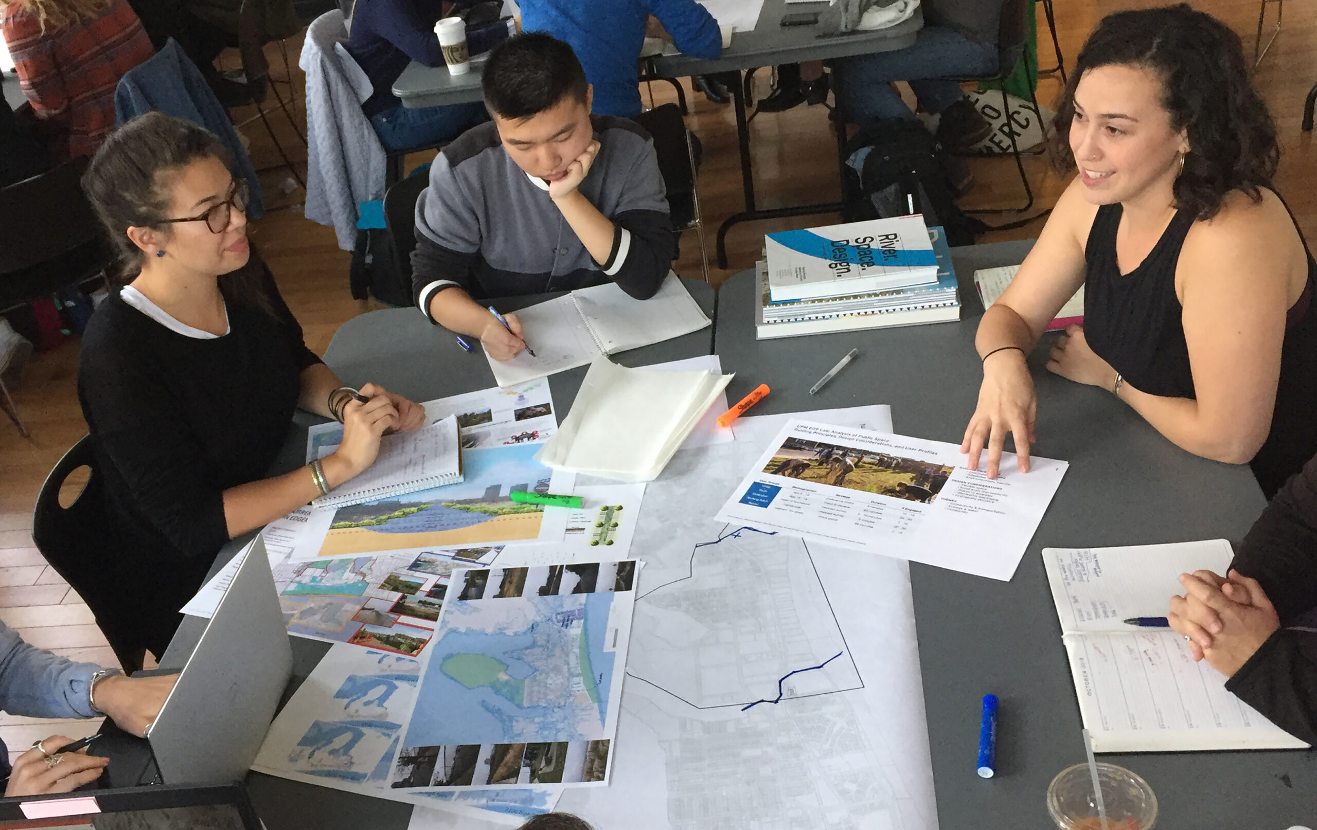 A group of people working together at a table. There are printouts of charts and designs on the table.