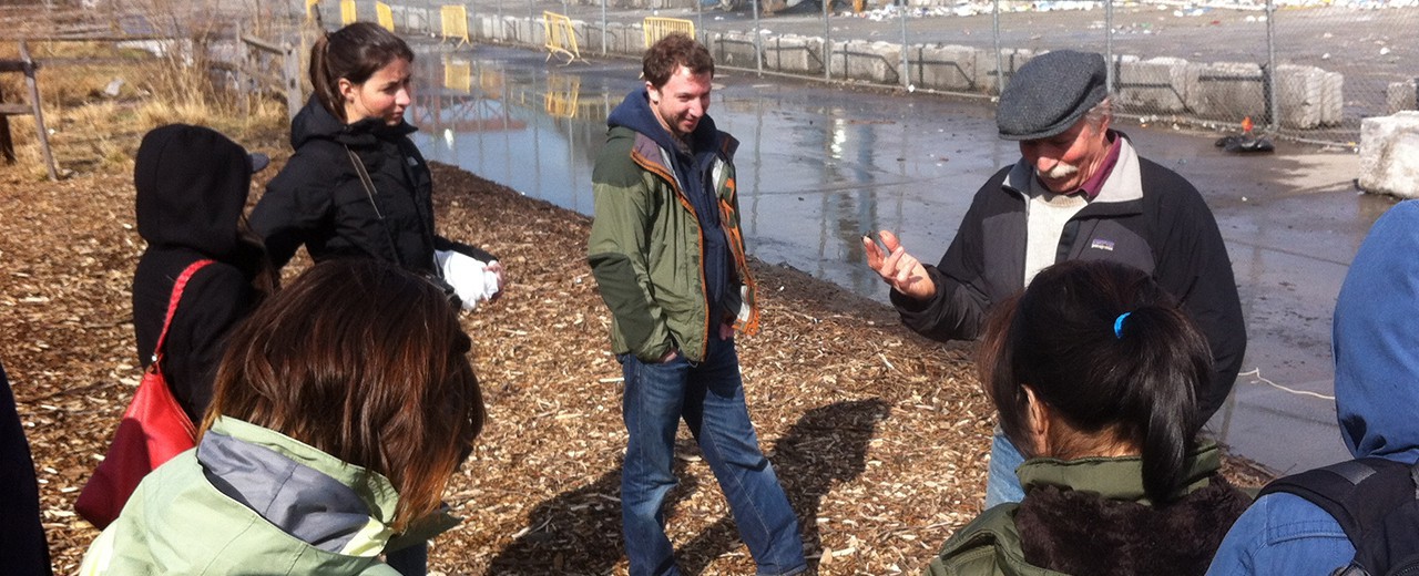 A professor stands in front of a group of students as they listen to him describe the construction site they are surveying.